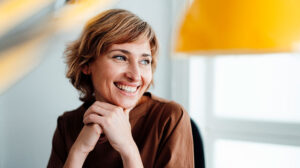 A Black woman holds a smartphone and smiles about the complimentary leadership affirmations calendar and leadership advice from the Center for Creative Leadership